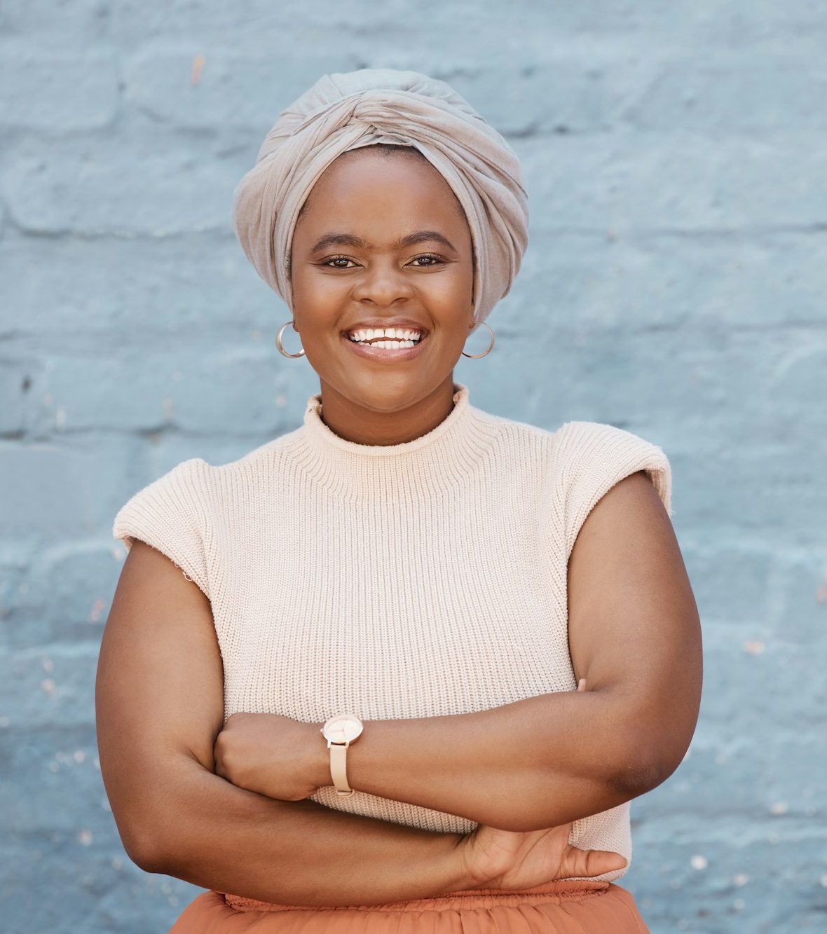 One smiling African American businesswoman with headscarf posing with arms crossed against a grey b