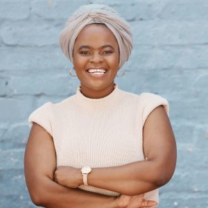 One smiling African American businesswoman with headscarf posing with arms crossed against a grey b